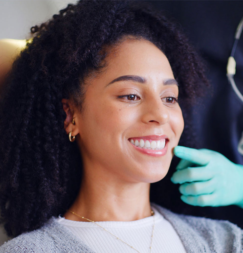 Woman smiling in dentist chair while dentist is wearing green glove